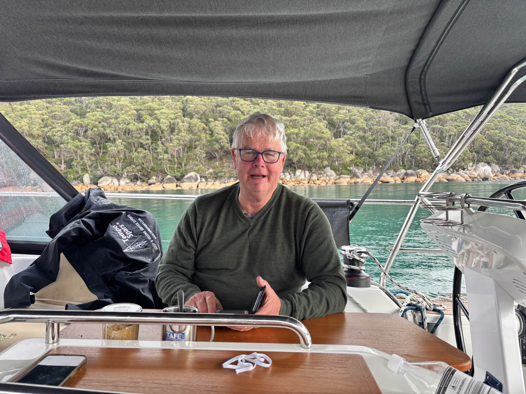 Owner John Corrie sitting at the teak cockpit table of his Hanse 458 yacht, Time Out X2, enjoying a cup of coffee while anchored in the calm waters of Refuge Cove at Wilsons Promontory.
