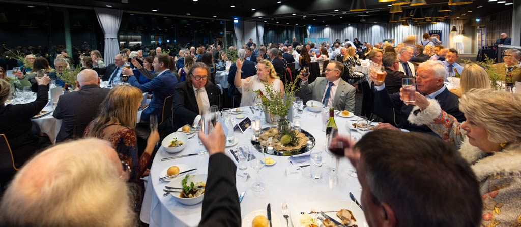 Wide shot across the room at the ORCV annual presentation night, with guests at every table raising their glasses in celebration