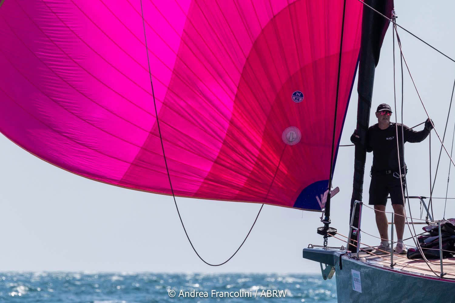 Bowman Shaun McKenna on the bow of Solaris 50 yacht Salt in black uniform with pink spinnaker flying to port.